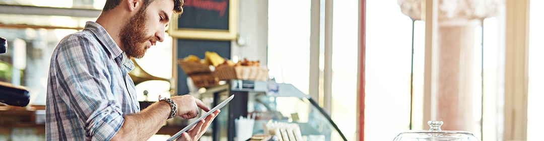 Image of a male employer using a tablet in a cafe.