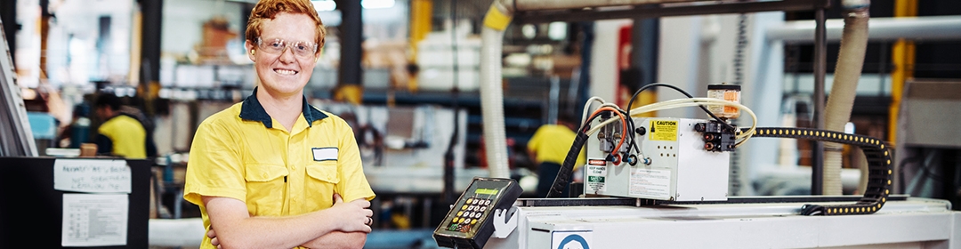 Image of a young apprentice working in a factory smiling at the camera.