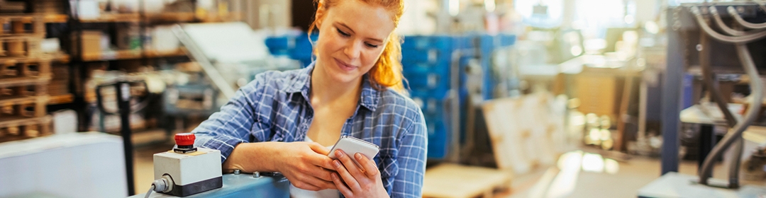 Image of a young female employee using her phone in a factory warehouse.